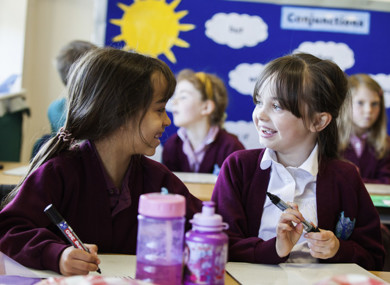 Two pupils, sat at their desks, smiling at each other.